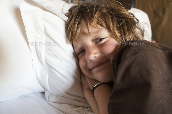 A smiling 5 year old boy in bed in his tent, Kalahari Desert.
