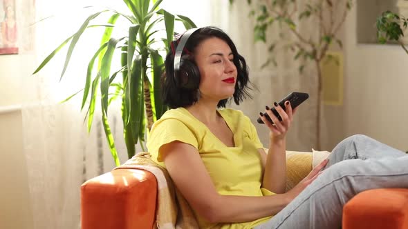 Woman in hedphones, lyuing on sofa, use virtual commands assistant on smartphone
