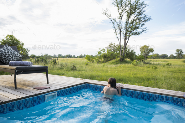 A boy in a swimming pool looking out at the landscape around a safari camp