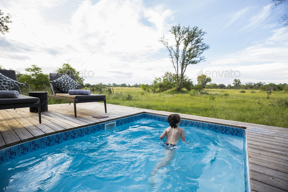 A boy in a swimming pool at a safari camp, looking out over the landscape