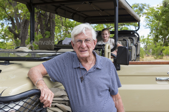 A senior man standing by a safari jeep smiling.