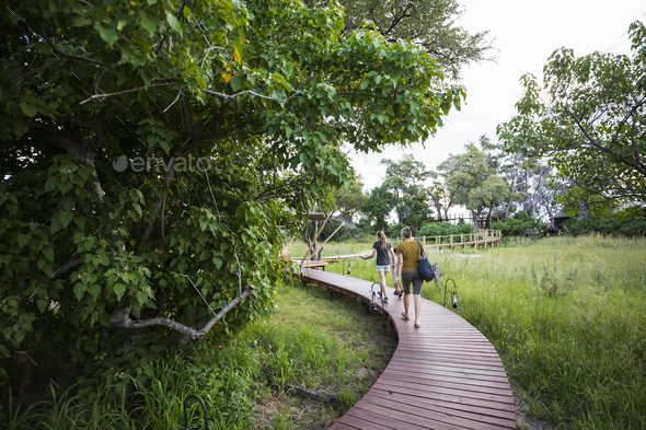 Two people, mother and teeage daughter walking on wooden path at a tented safari camp