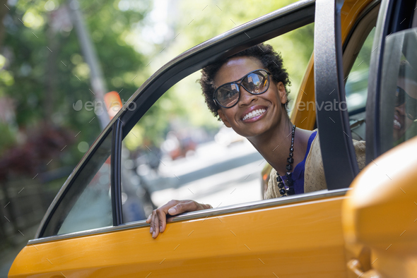 City life. People on the move. A woman getting out of the rear passenger seat of a yellow cab.