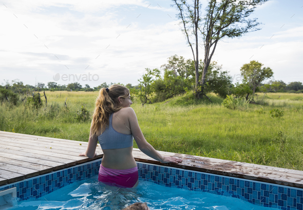 A teenage girl in a swimming pool looking out at the landscape around a safari camp