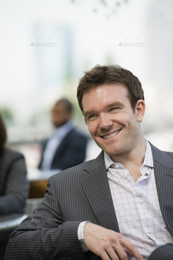 Business man with open collar and jacket sitting on a bench.