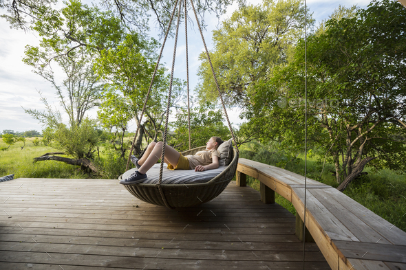 13 year old girl resting in large swing on a deck at a safari camp.