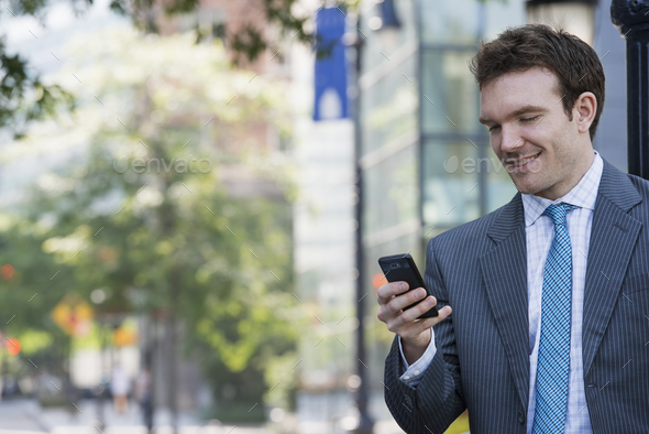 Summer in the city. Businesspeople outdoors, on the go. A young man in a grey suit and blue tie. Using a smart phone.