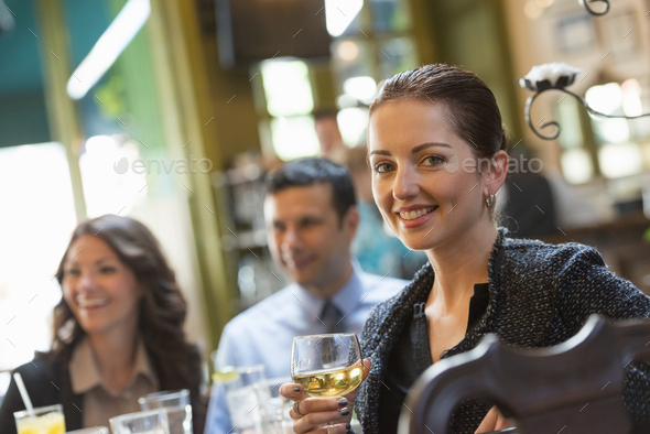 Business people outdoors, keeping in touch while on the go. Three people around a cafe table, one woman turning around, holding a wine glass.