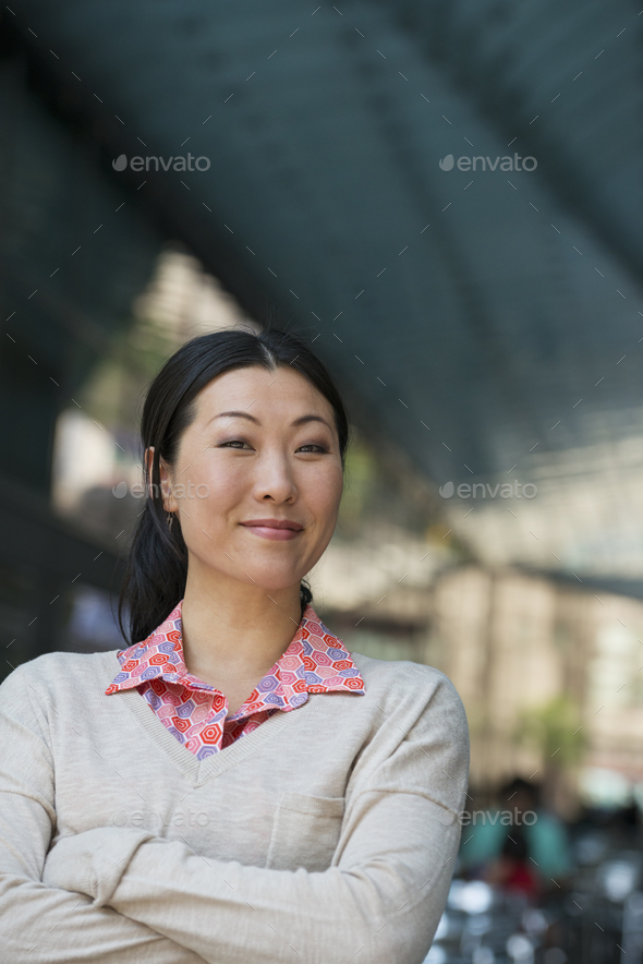 Outdoors in the city. In a public space. Business people on the move. A woman in a pink shirt and beige sweater.