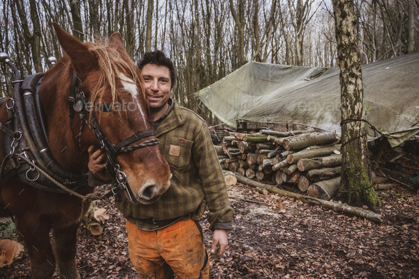 Portrait of a logger, standing in a forest camp with one of his work horses.