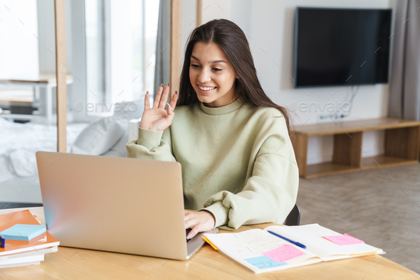 Photo of student woman waving hand and using laptop while doing homework
