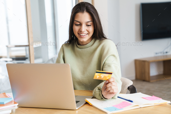 Photo of woman holding credit card and using laptop while doing homework