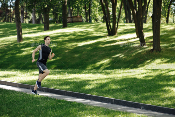 Urban sport and outdoor training. Muscular guy fitness tracker runs at path