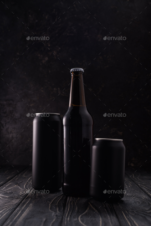 Bottle Between Black Metallic Cans of Beer on Wooden Table