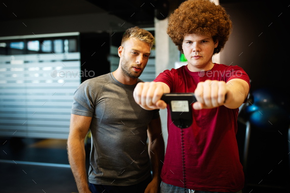 Fat young men with trainer exercising at fitness gym