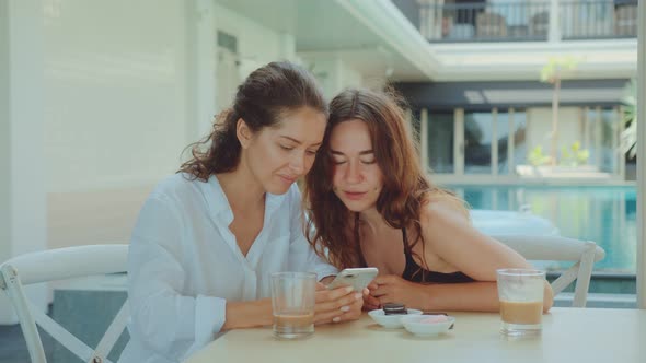 Two Beautiful Women Laughing While Using a Smartphone While Drinking Coffee alt