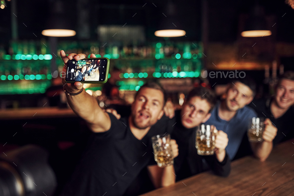 Making a selfie. Three friends resting in the pub with beer in hands. Having conversation