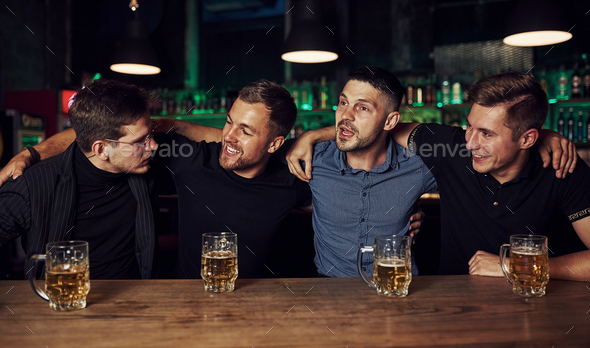 Three friends resting in the pub with beer in hands. Having conversation