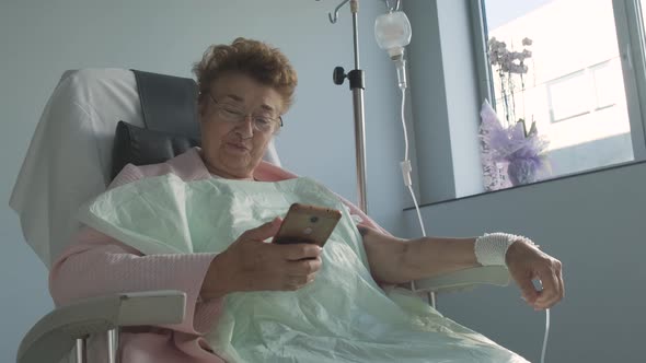 Smiling Senior Lady Having Video Call On Cellphone While Resting In The Hospital. medium shot alt