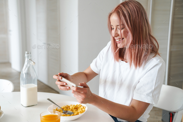Photo of woman playing online game on cellphone while having breakfast