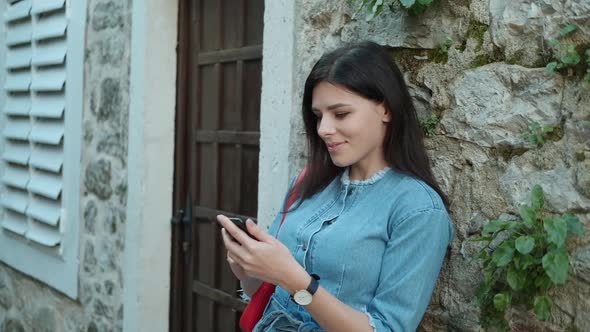 Pretty young woman with brunette hair in denim overalls  texting on her phone alt
