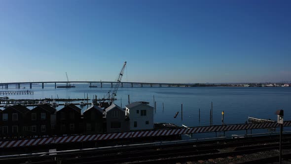 A drone shot of elevated train tracks near a bay in Queens, NY. The camera boom up over the tracks & alt