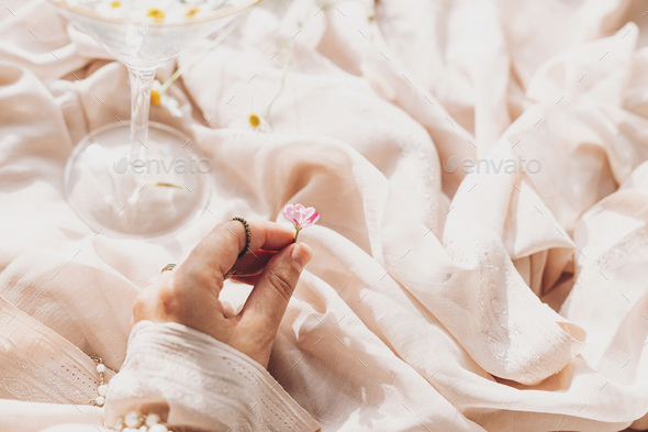 Hand with jewelry holding pink flower on background of soft beige fabric