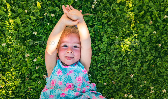 Beautiful baby girl lying on grass laughing and looking up