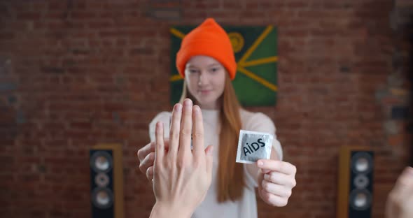 Young Woman Showing Condom with Stop Aids Inscription at Camera and Unrecognizable Hands Cover Them alt