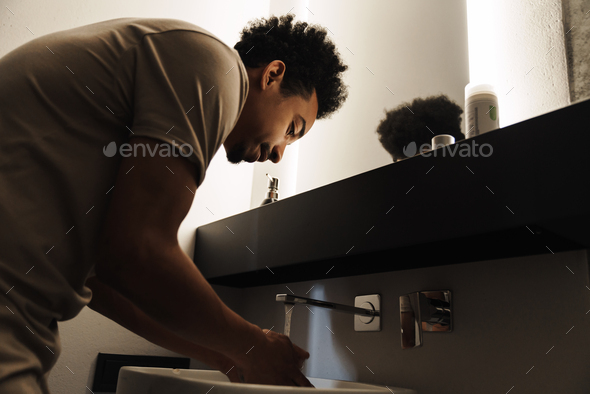 Photo of young african american man cleaning his face in front of mirror