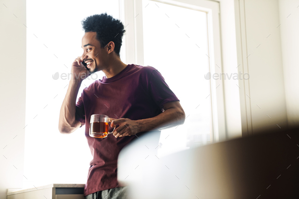 Photo of african american man drinking tea while talking on cellphone