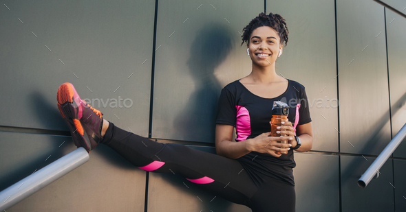 African american young woman in sportswear with wireless headphones and fitness tracker holding