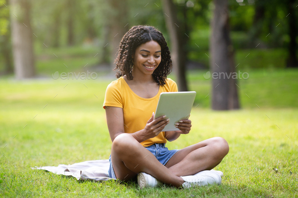 Online communication, education or work. Pretty African American lady with tablet computer at park