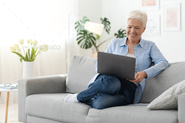 Home Relax. Positive Elderly Woman Resting With Laptop On Couch, Watching Movies