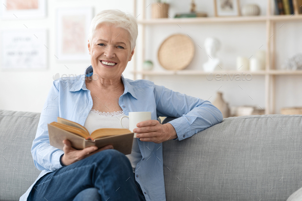 Book Lover. Smiling Senior Woman Enjoying Reading, Relaxing On Couch At Home