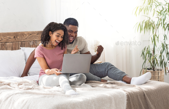 Emotional black couple looking at laptop screen and screaming