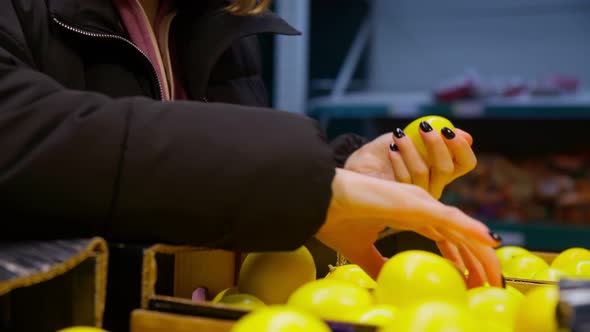 Hands of the Girl Choose Fresh Lemon on the Shelves of the Hypermarket alt