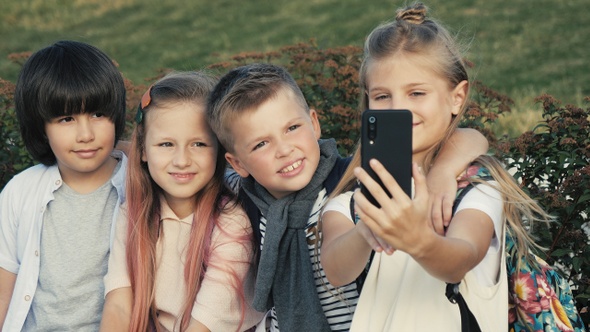 Pretty school children friends taking selfie on smartphone. alt