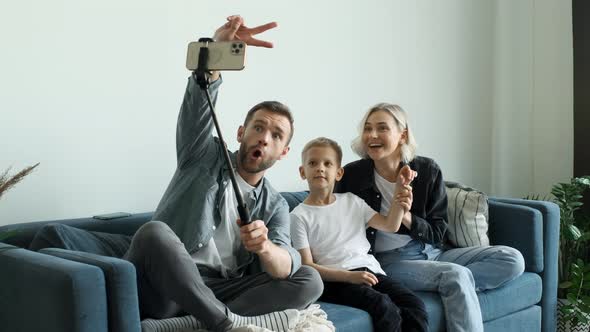 A Young Smiling Family Takes A Selfie on a Smartphone, Mom And Dad Are Sitting on the Sofa alt