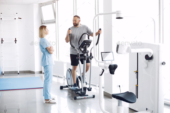 Patient doing exercise on spin bike in gym with therapist