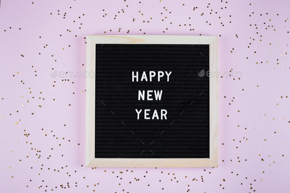 Flat lay with congratulation Happy New Year on letters board. Top view. Pink background with confetti