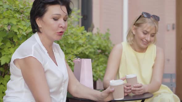 Portrait of Two Relaxed Carefree Women Chatting with Someone in Outdoor Cafe and Laughing. Positive alt