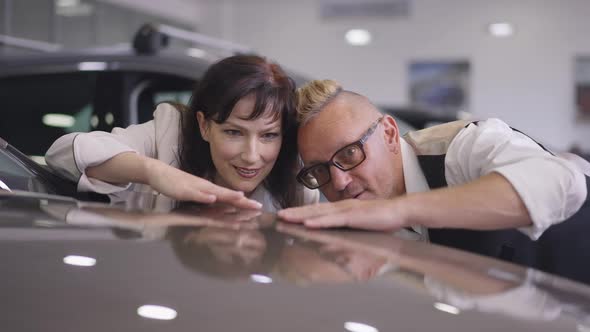 Portrait of Confident Successful Adult Couple Touching Luxurious New Car Hoods Talking in Slow alt