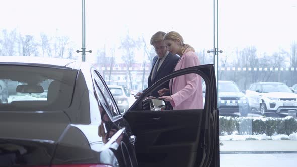 Young Bearded Businessman in Glasses and Wife Are Choosing a Car alt
