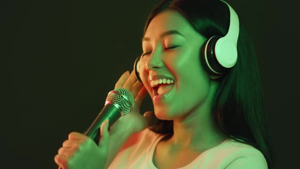 Young Asian Female Musician in Professional Headphones Singing Song to Mic at Sound Record Studio in alt