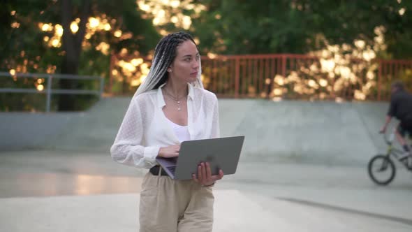 Elegant Young Woman with Black and White Dreadlocks Hair Walking By Park or Skatepark with Open alt