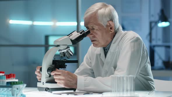 Senior Scientist Working with Microscope and Posing for Camera alt