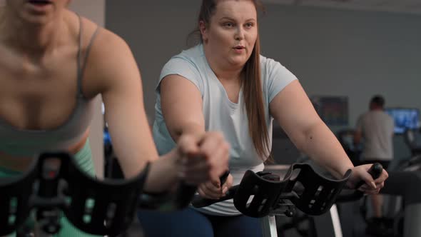 Two caucasian women ride a bikes at the gym. Shot with RED helium camera in 4K. alt