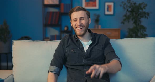 Relaxed Smiling Man Sits on the Sofa in the Living Room Dressed in a Plain alt