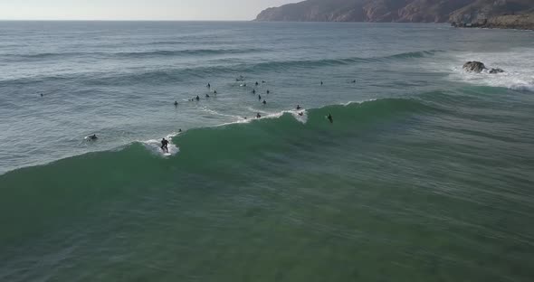 Aerial, reverse, drone shot of surfers waiting for waves,one riding a wave, on a sunny evening, Casc alt